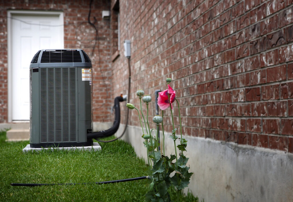 High-efficiency modern HVAC unit next to a brick home, with pink flowers in foreground.