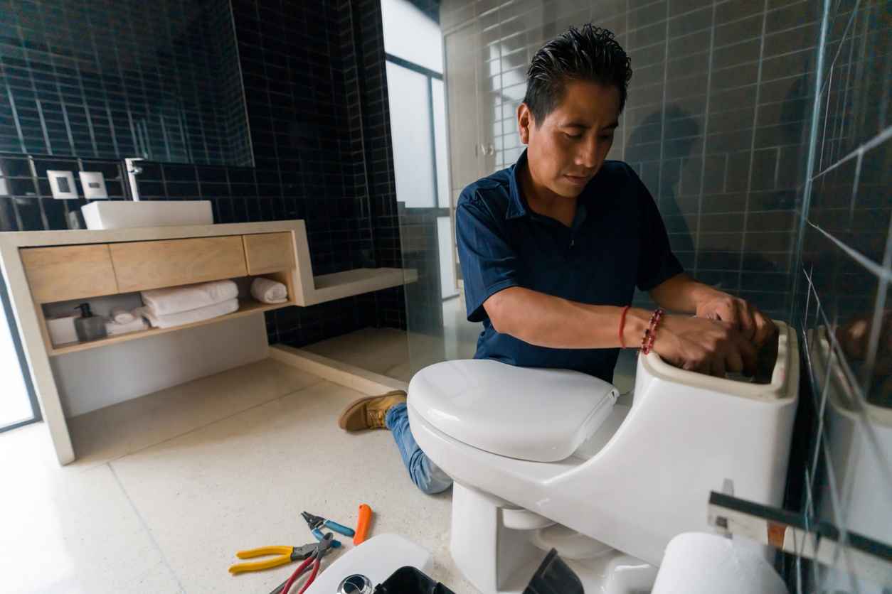 Latin American plumber fixing a toilet in the bathroom - home repair concepts