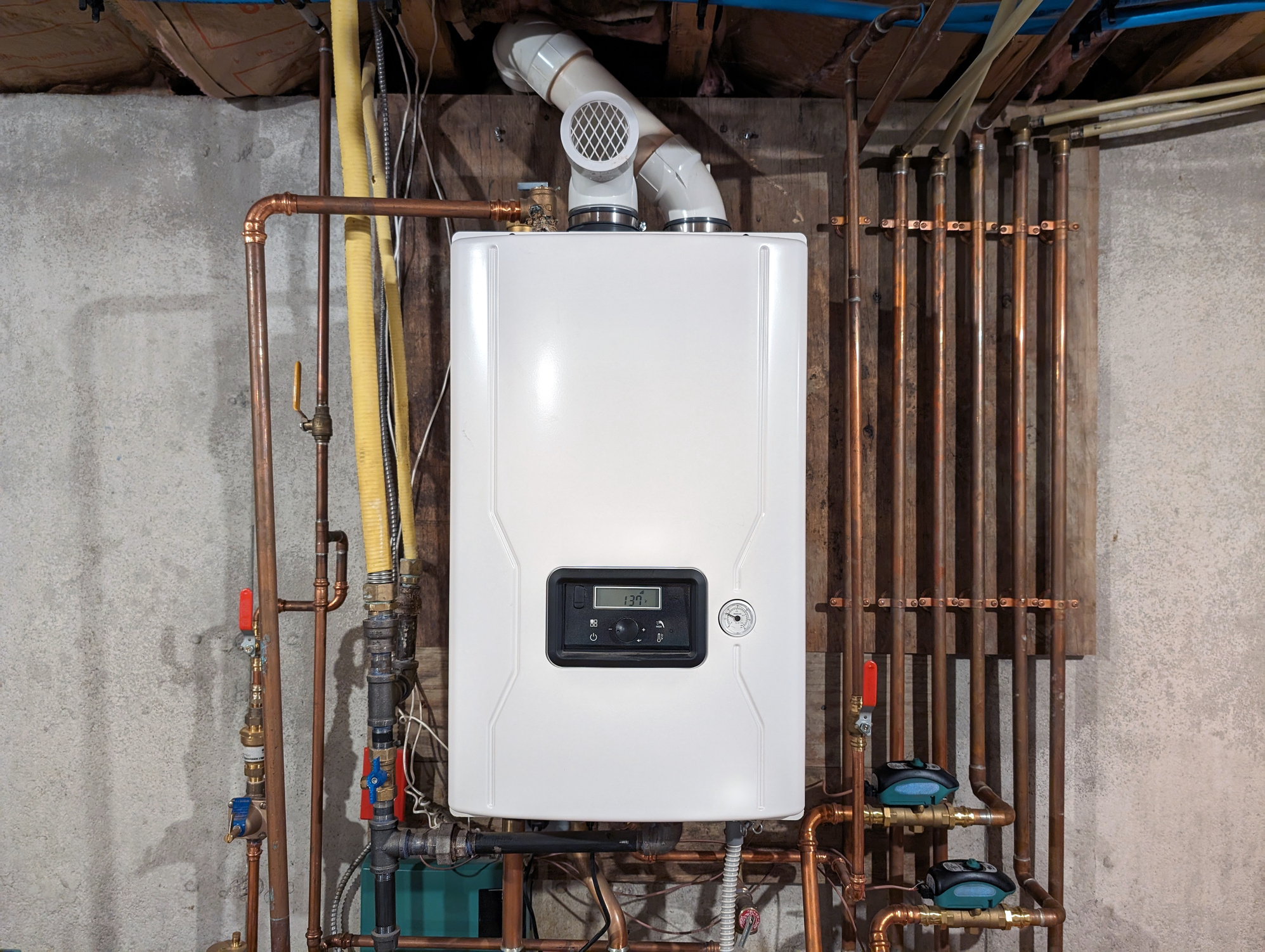 Straight-on color shot of a Tankless Water Heater installed on a well-lit basement wall of a residential building.
